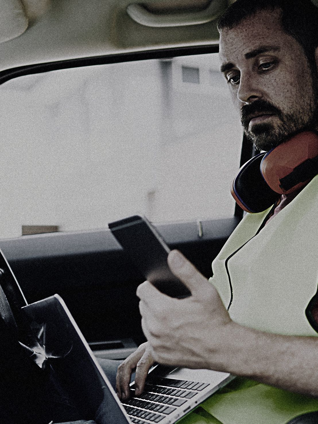 A man wearing headphones sits in a car using a laptop