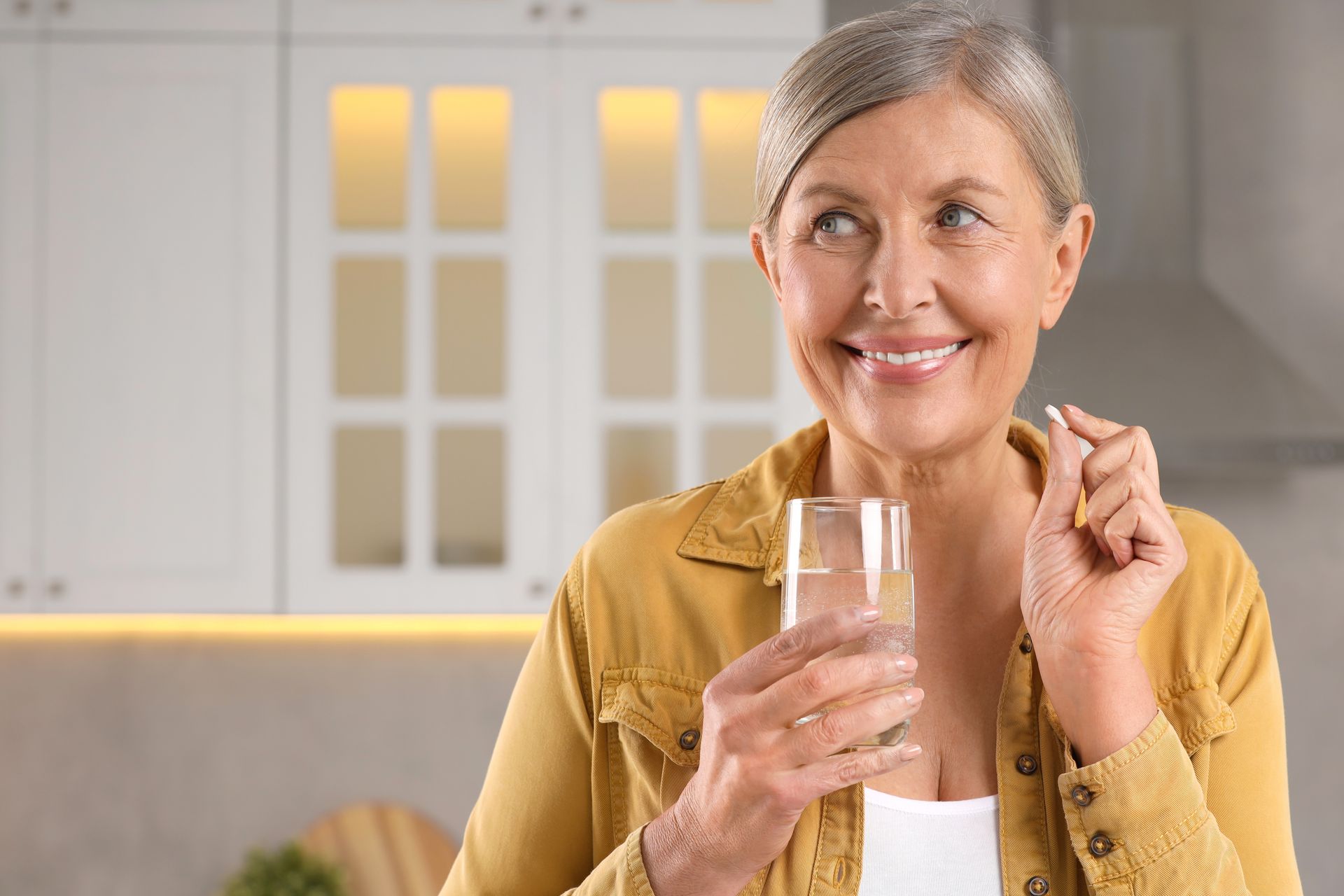 An elderly woman is taking a pill and drinking a glass of water.