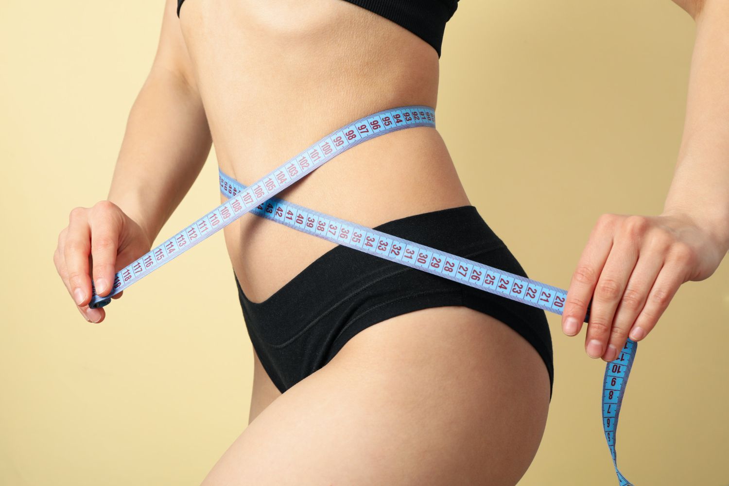 A woman is measuring her waist with a tape measure.