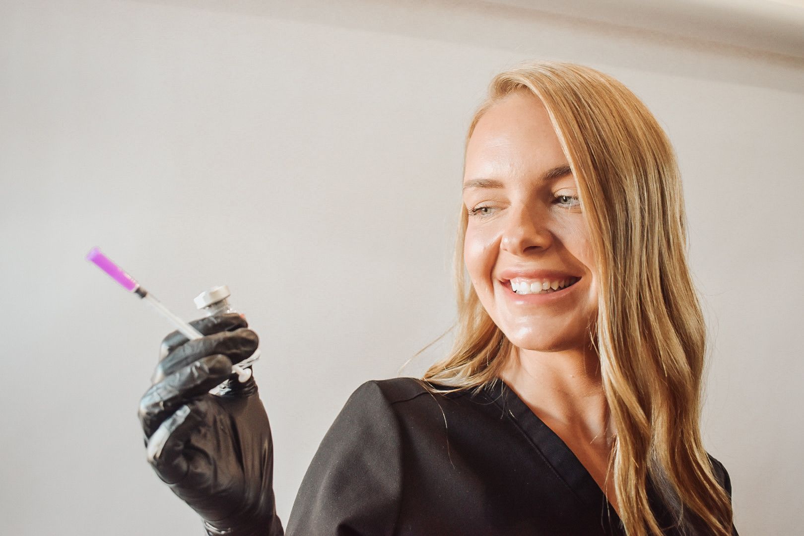 A woman is smiling while holding a syringe in her hand.