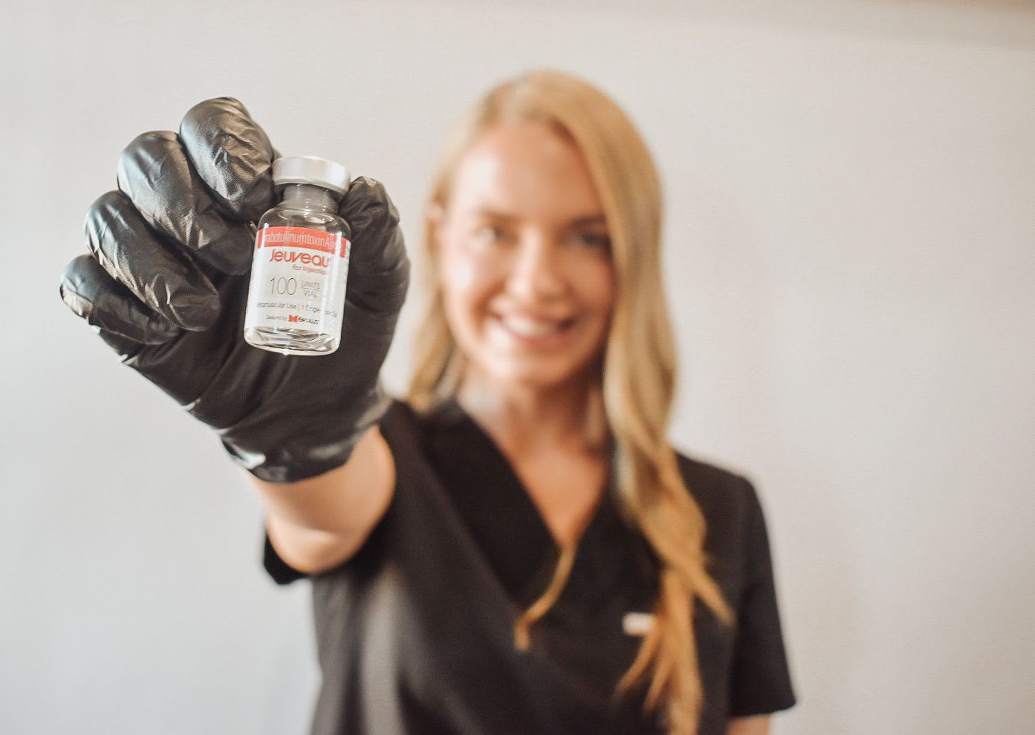 A woman wearing black gloves is holding a bottle of liquid in her hand.