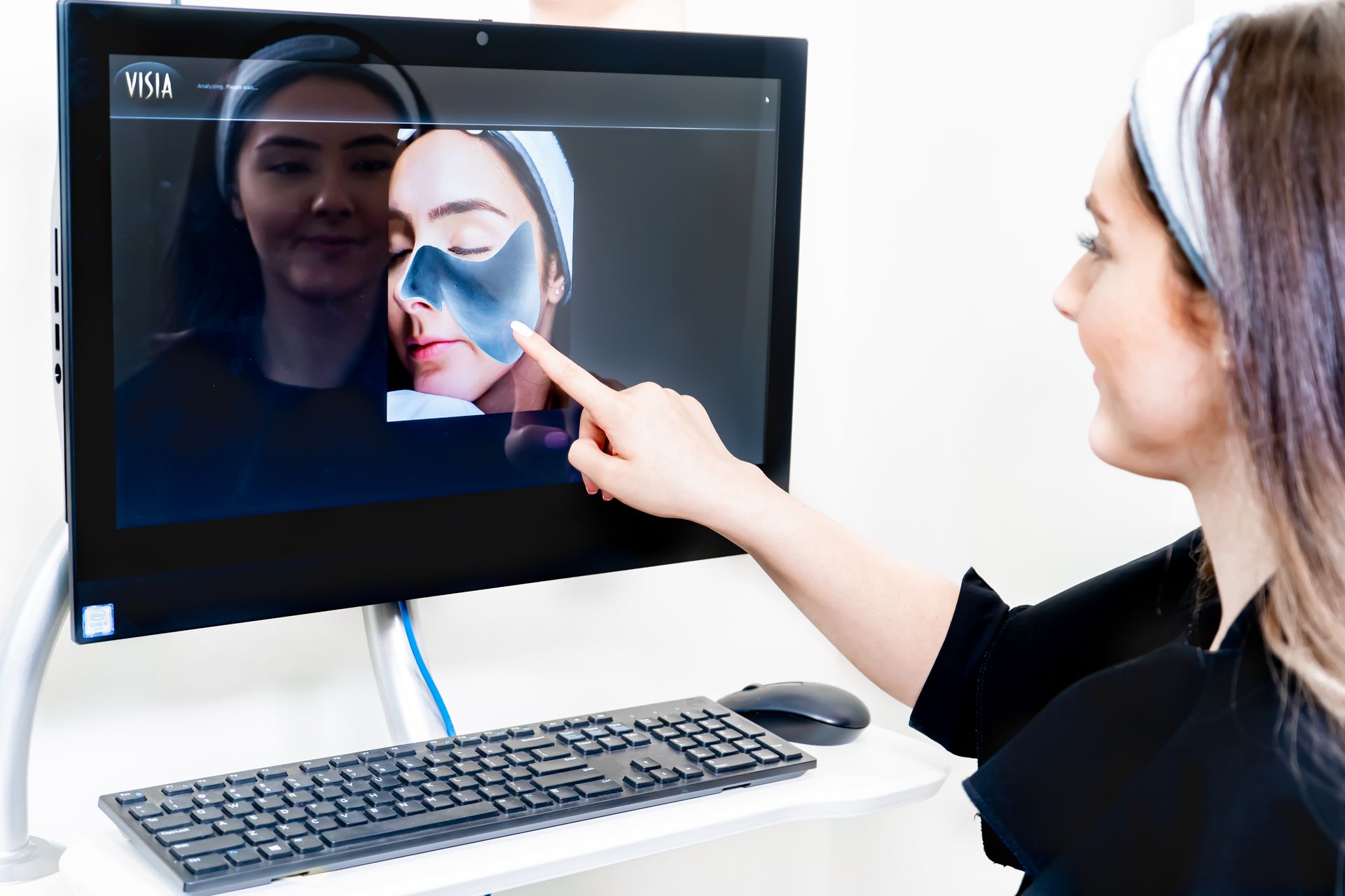 A woman is pointing at a picture of a woman 's face on a computer screen.