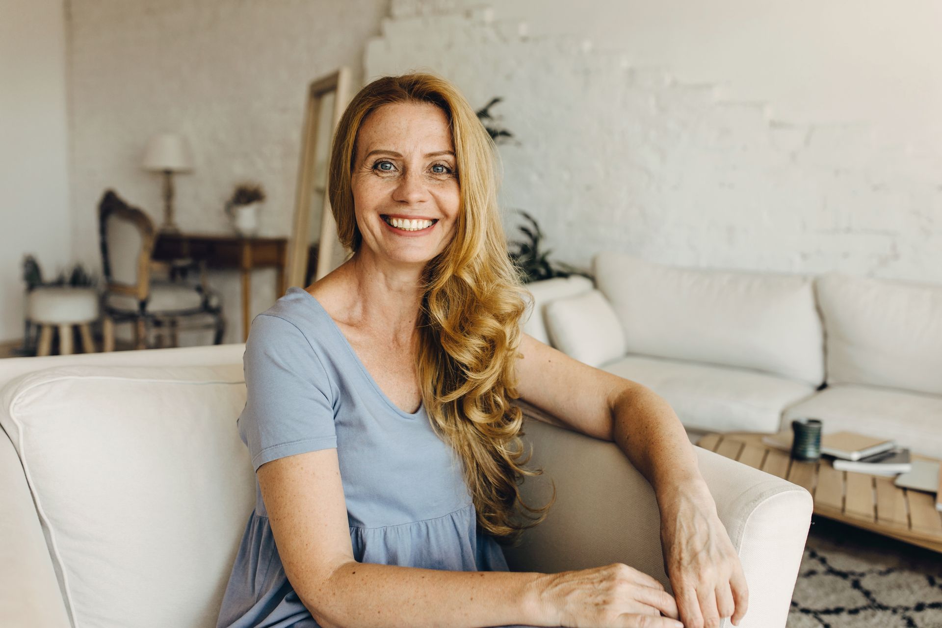 A woman is sitting on a couch in a living room smiling.