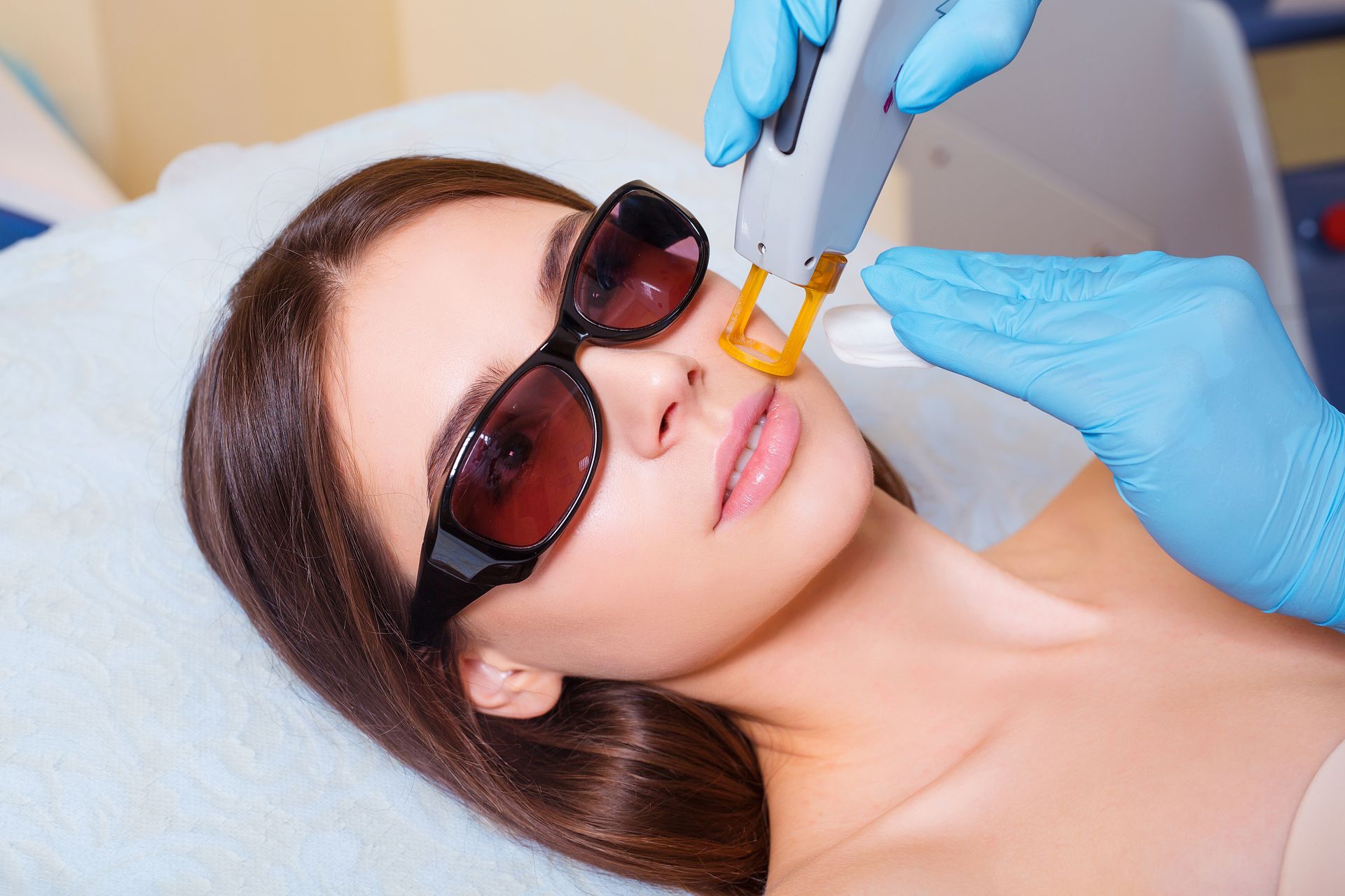 A woman wearing sunglasses is getting a laser hair removal treatment on her face.