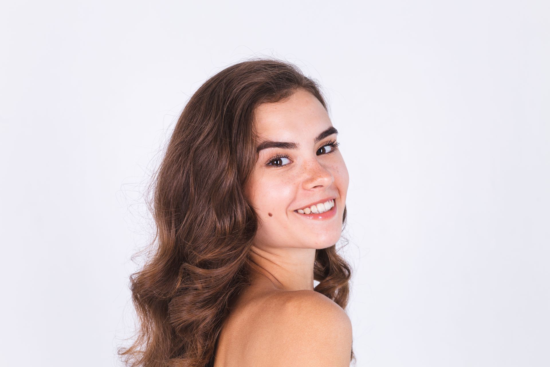 Young woman with curly brown hair smiles over her shoulder.