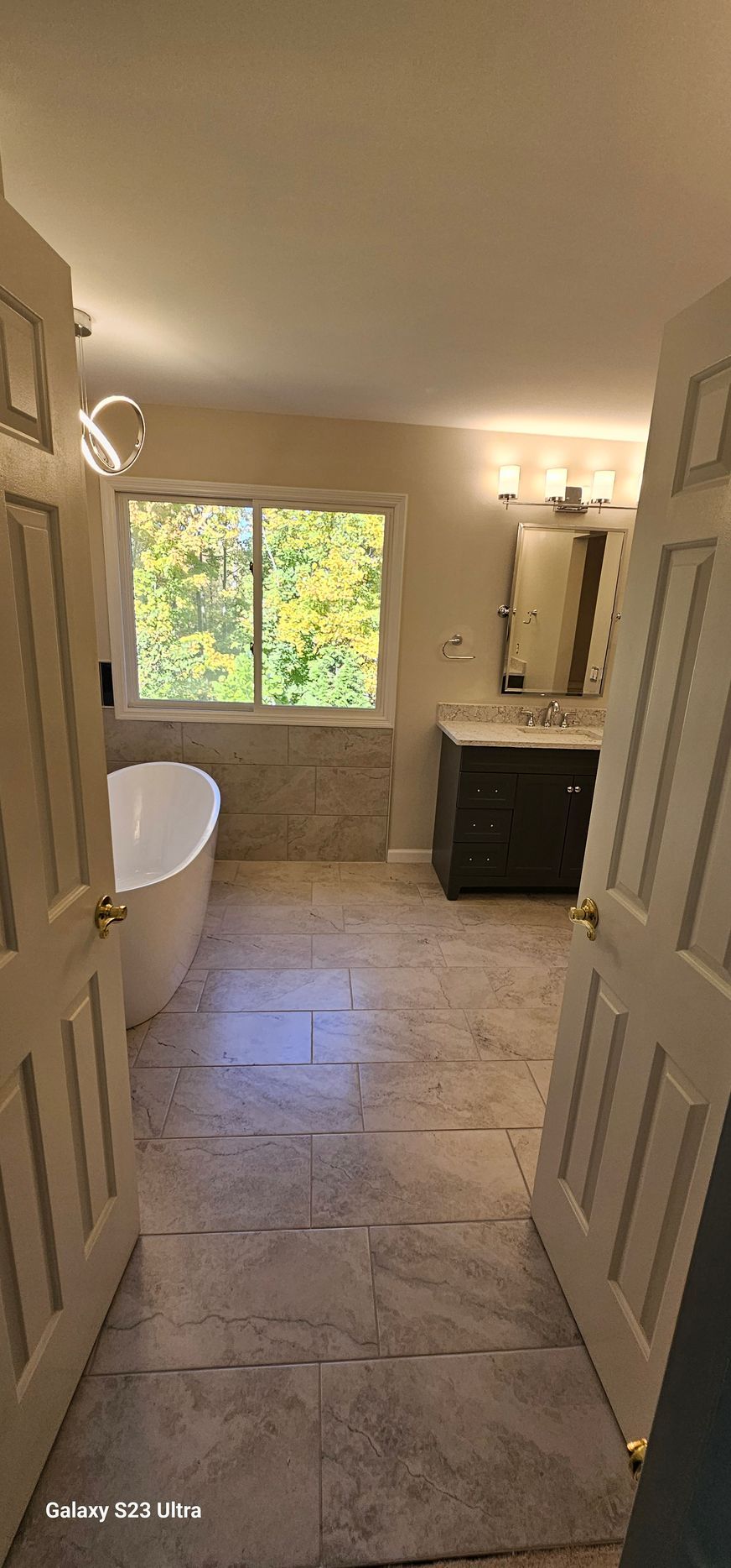 A bathroom with a tub , sink , mirror and window.
