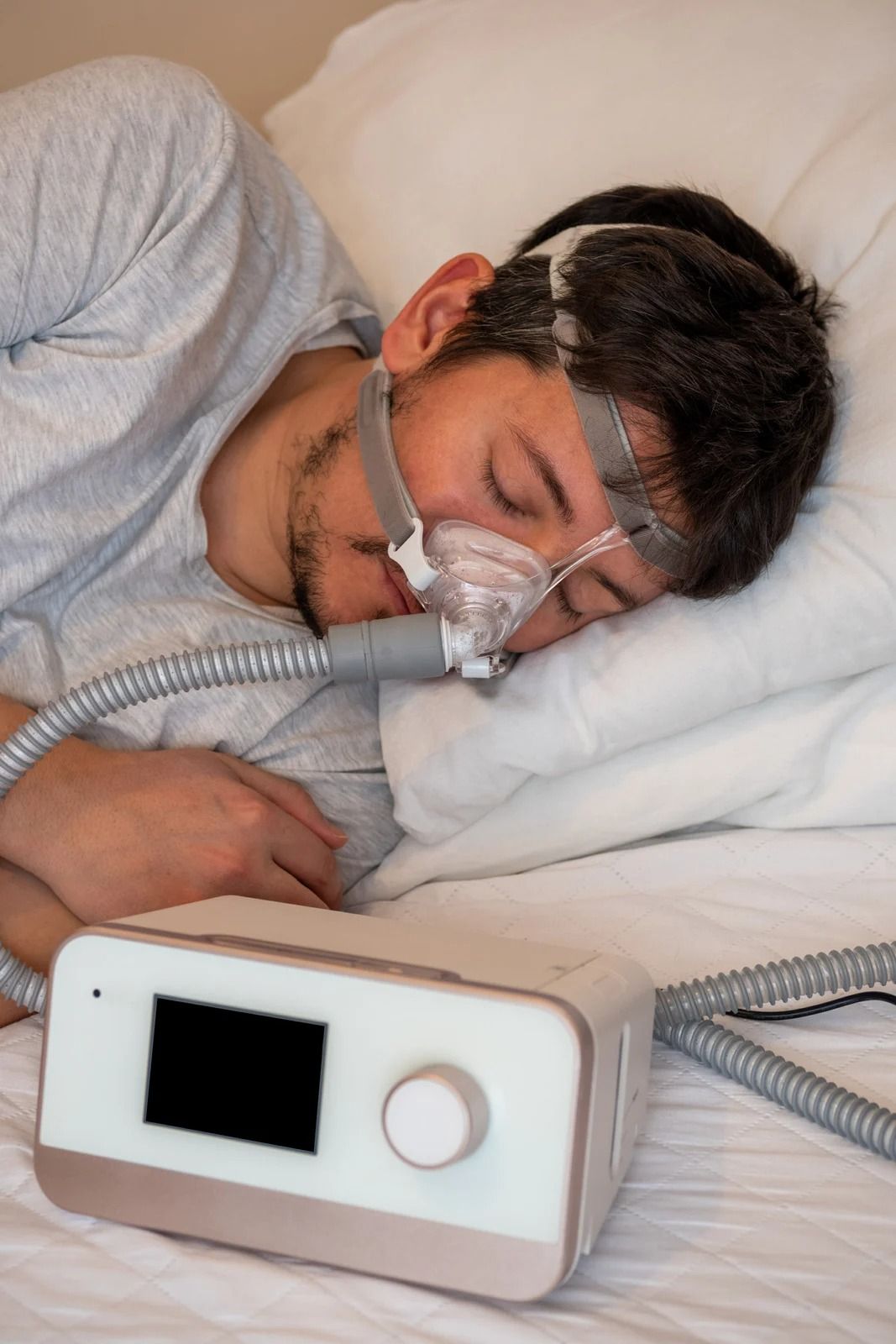 A person sleeps on their side wearing a nasal CPAP mask connected to a bedside machine.