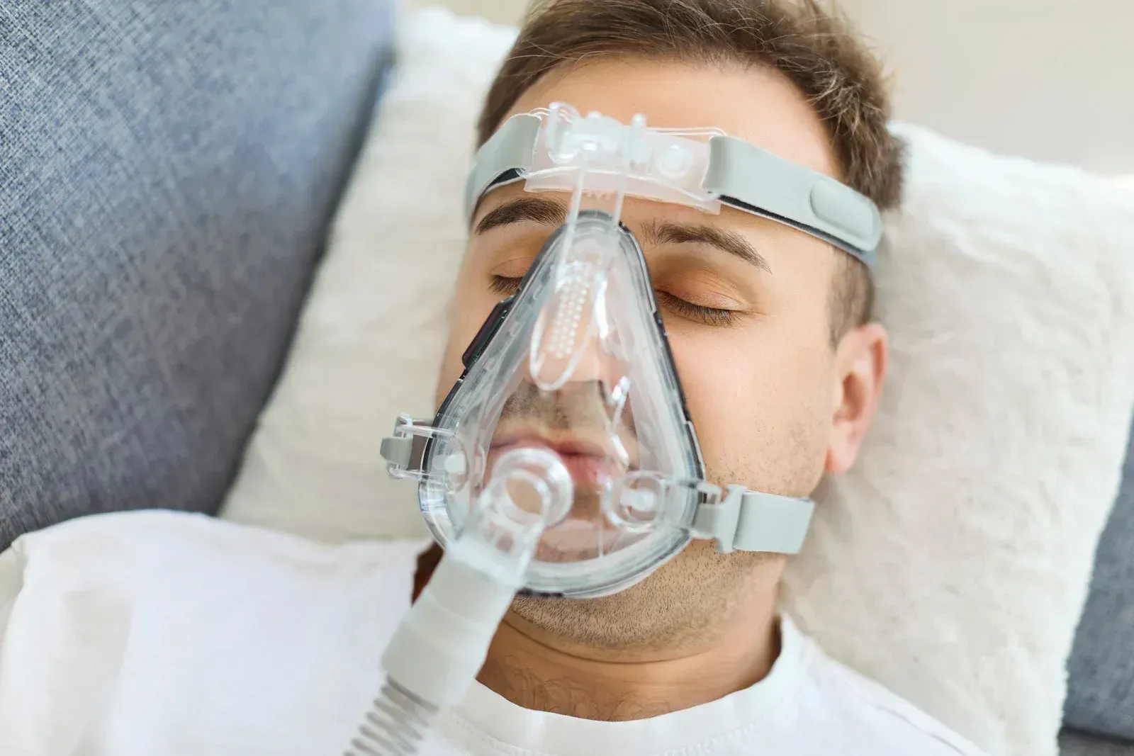 A person resting on a pillow while wearing a CPAP mask connected to a hose for sleep apnea therapy.