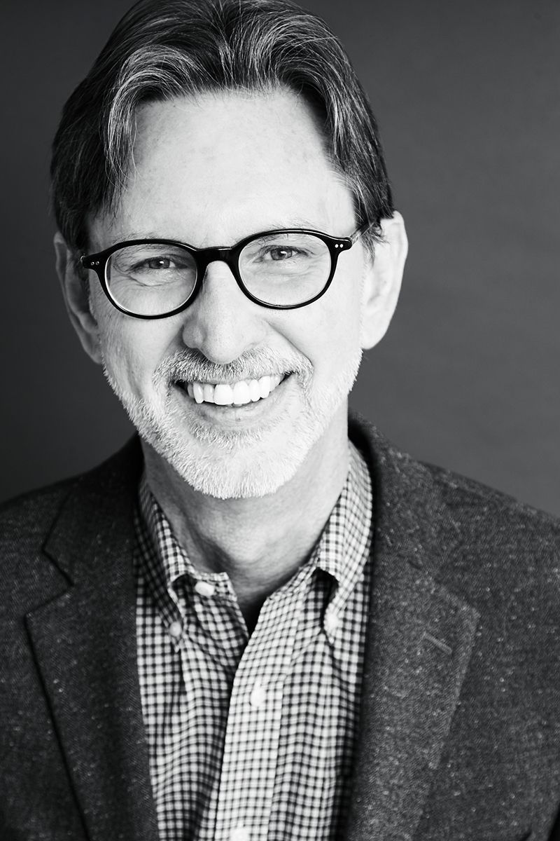 A man wearing glasses and a suit is smiling in a black and white photo.