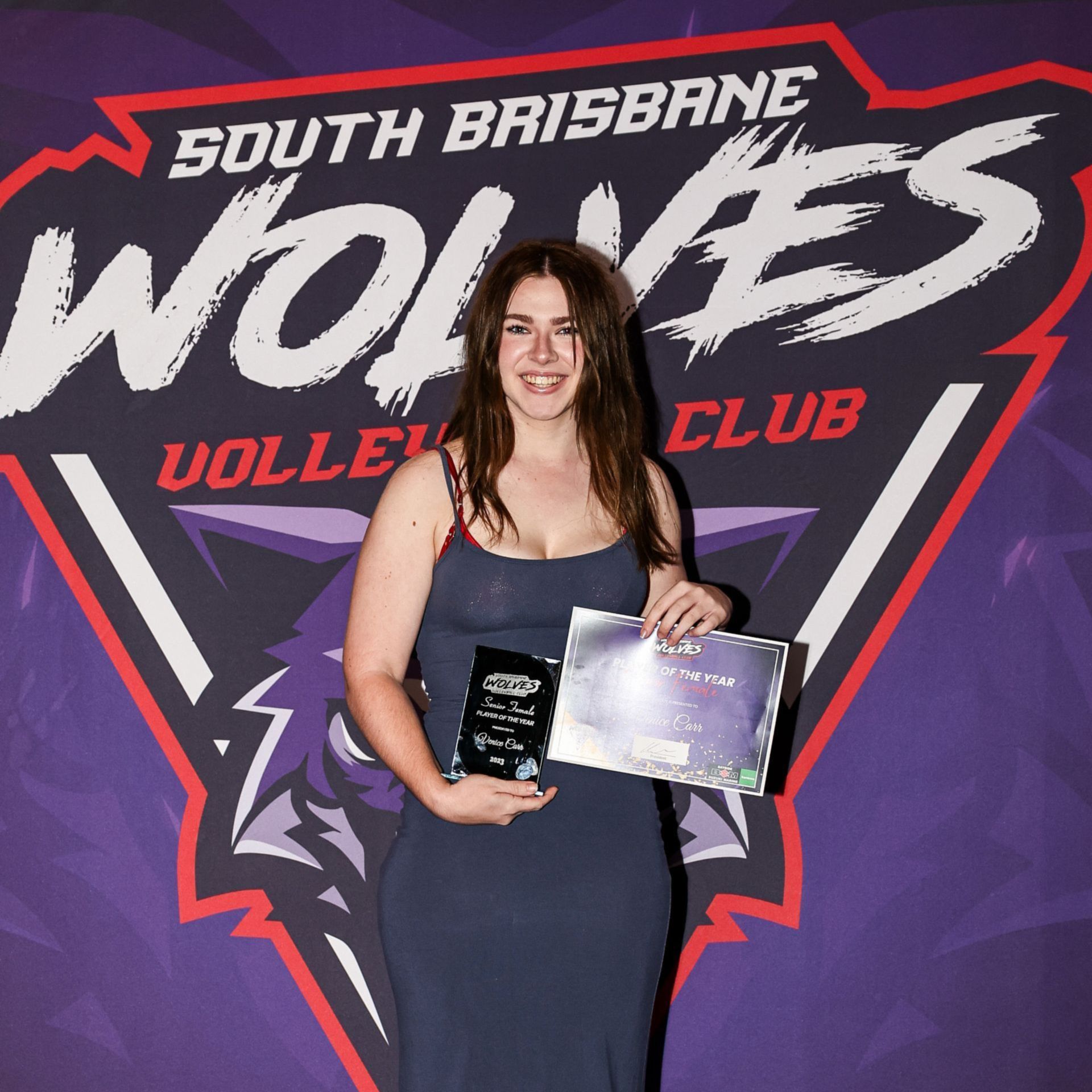 A woman holding an award in front of a south brisbane wolves logo