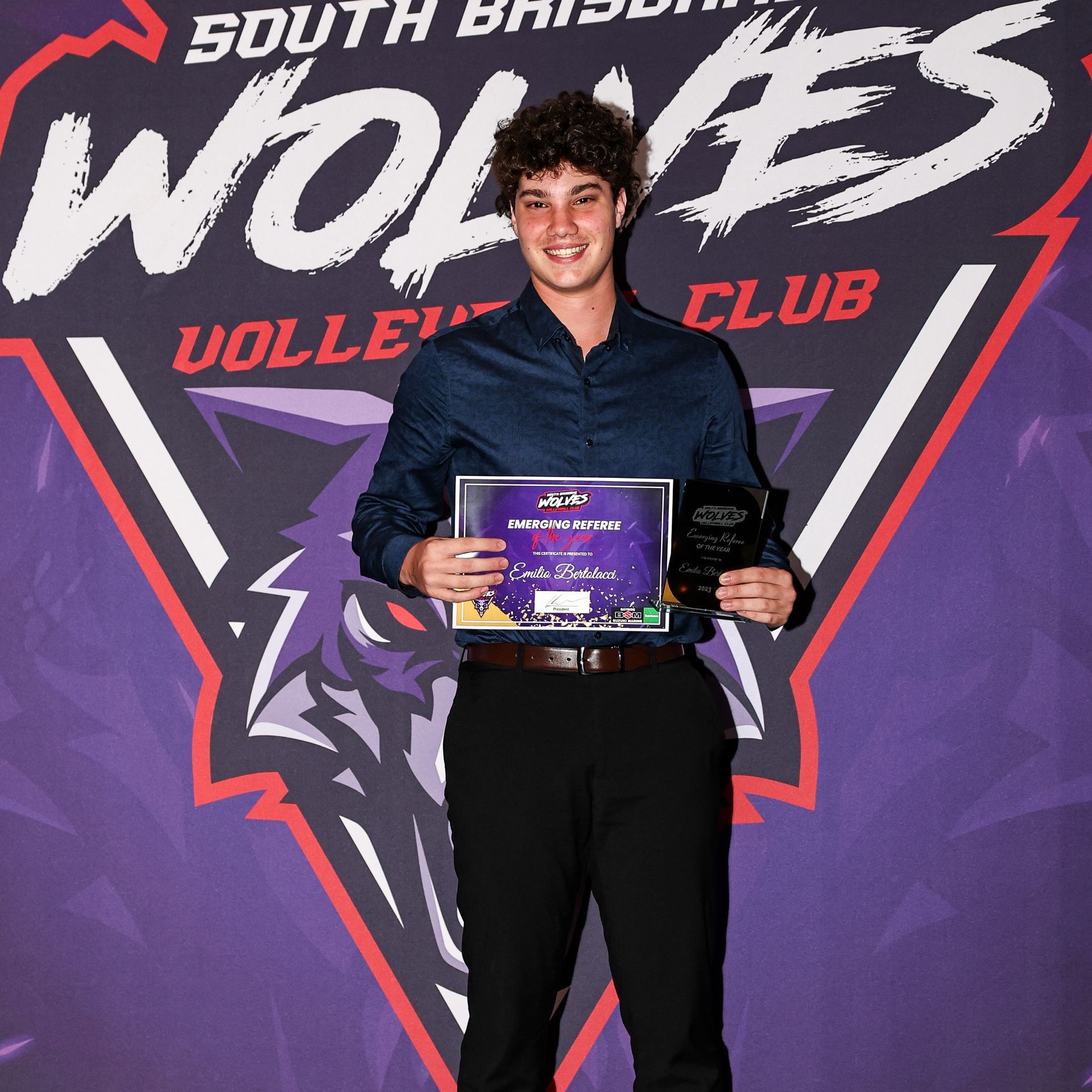 A young man is holding a certificate in front of a south brisbane wolves club logo