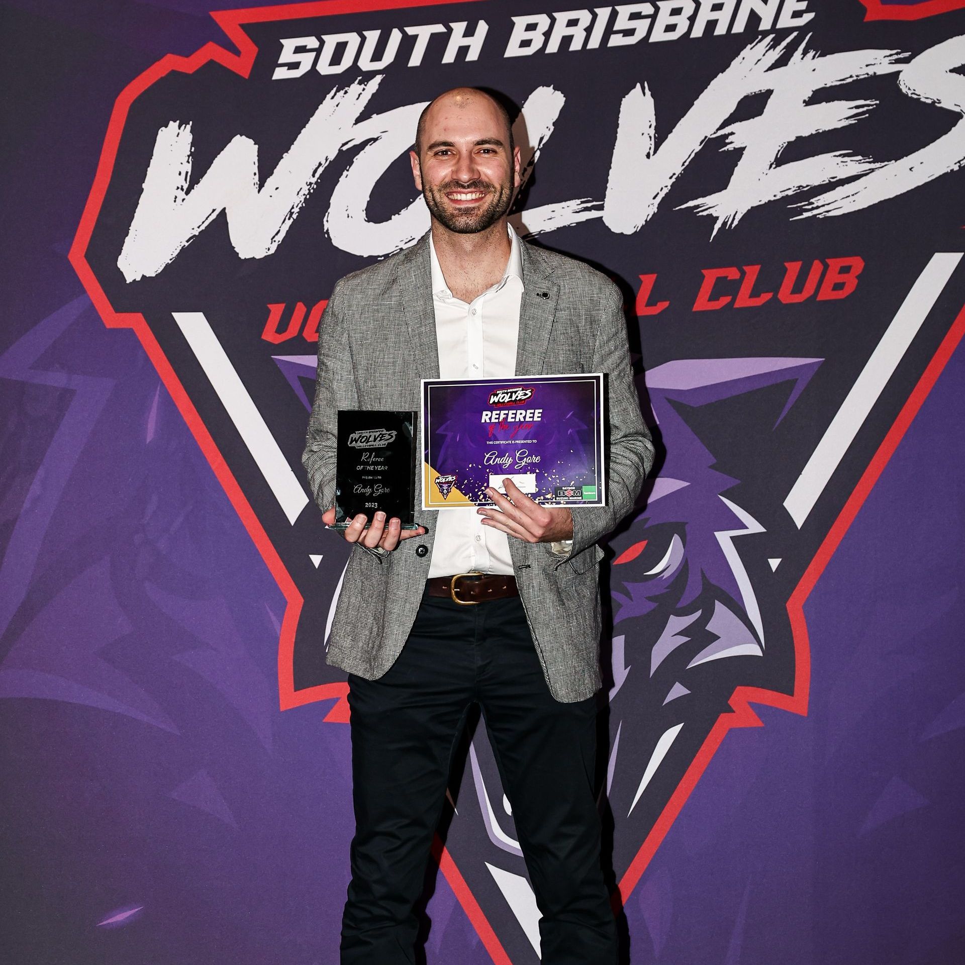 A man is holding a certificate in front of a south brisbane wolves logo