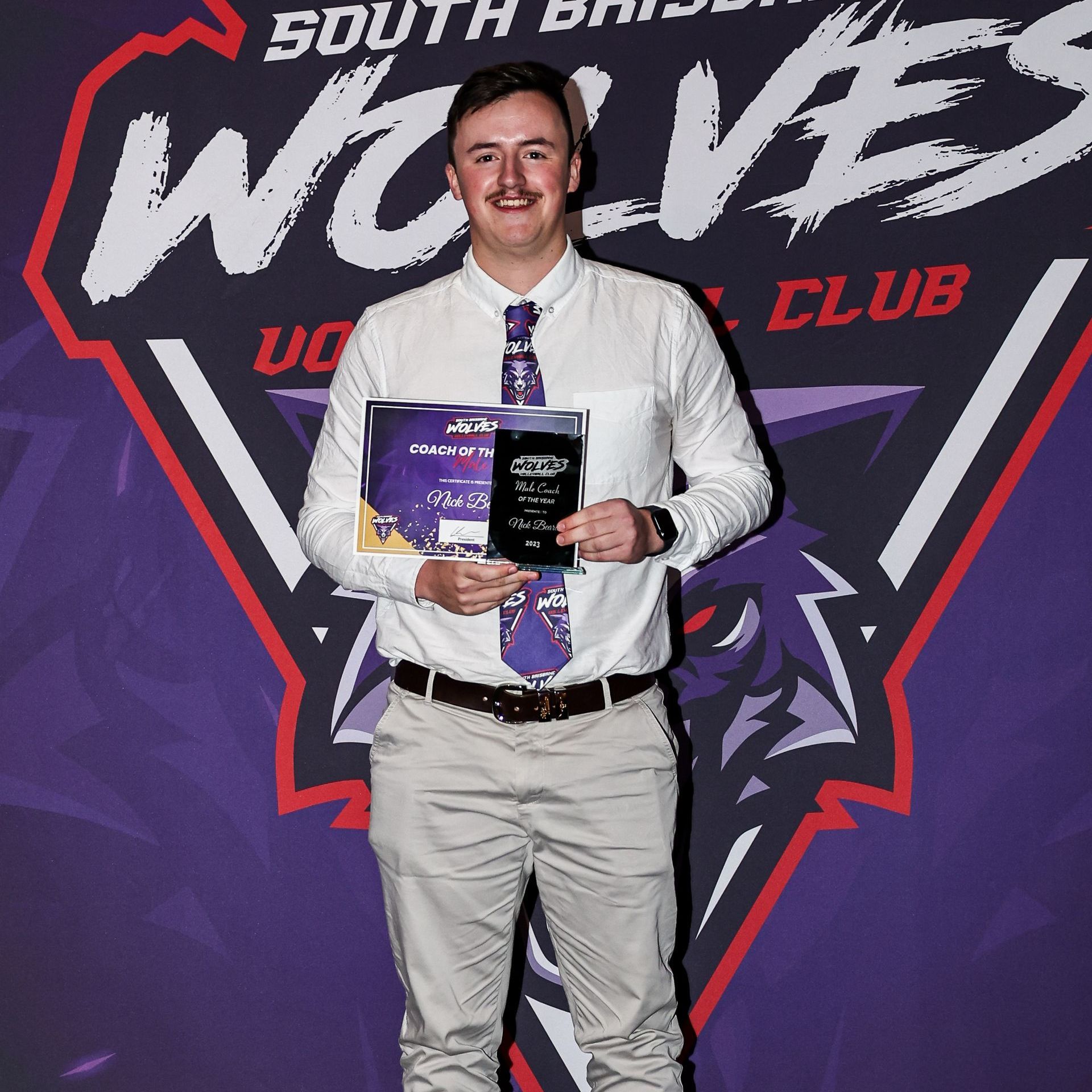 A man holding a certificate in front of a south brisbane wolves club logo