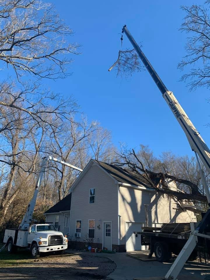 Crane hoisting roof materials beside a beige house with a white truck and leafless trees under a blue sky