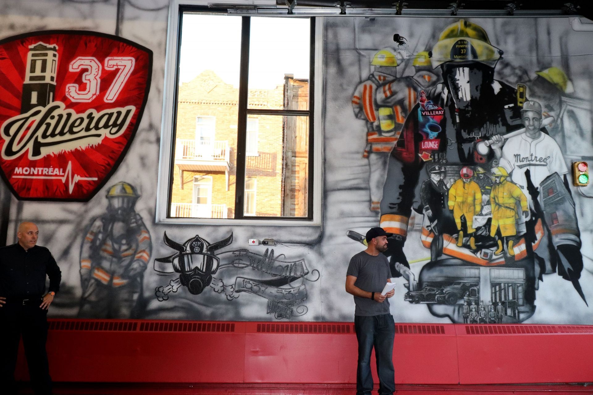 Un homme se tient devant un mur avec une fresque de pompiers dessus.