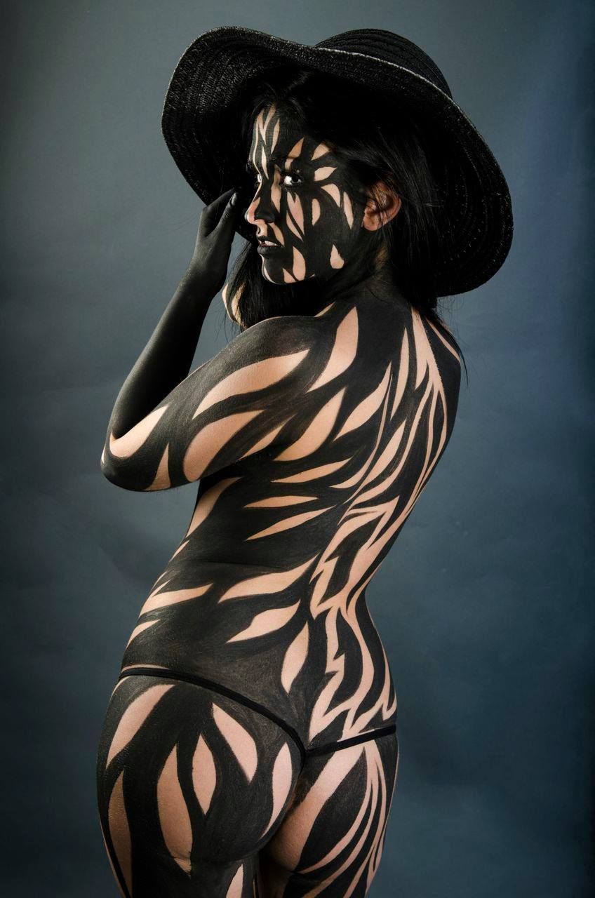Une femme dont le corps est peint en noir et blanc porte un chapeau.
