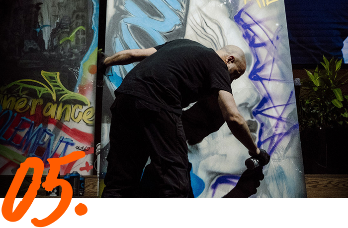 A man is spray painting graffiti on a wall with the number 05 below him