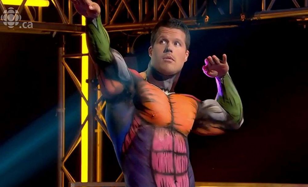 Un homme dans un costume de super-héros peint sur le corps se tient sur une scène.