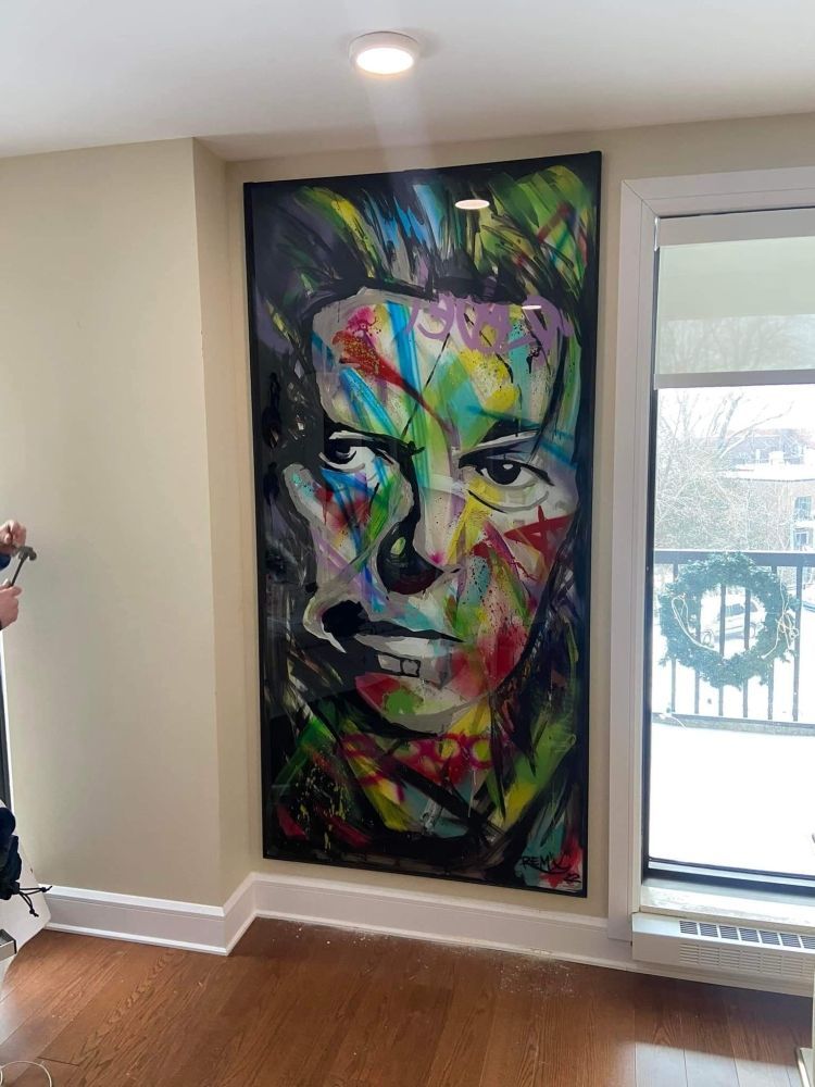 Un grand tableau représentant le visage d'un homme est accroché sur un mur à côté d'une fenêtre.