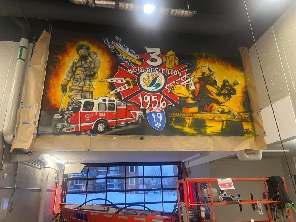 Une fresque de pompiers est en train d'être peinte sur le mur d'une caserne de pompiers.