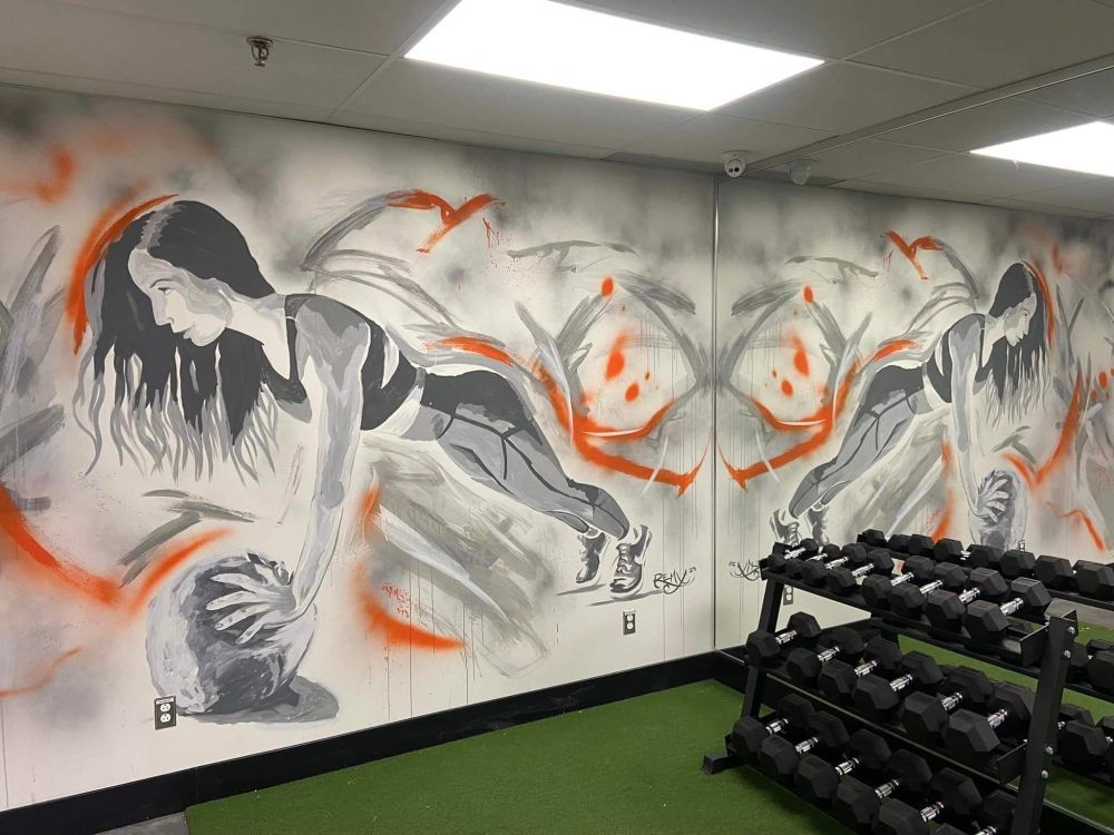 Une salle de sport avec une peinture murale sur le mur représentant une femme tenant un ballon.