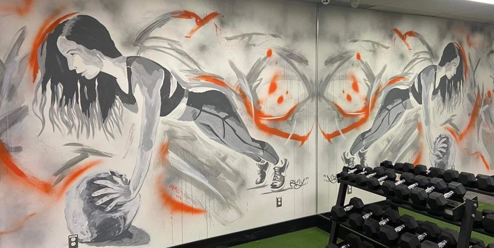 Il y a une peinture murale d'une femme faisant des pompes sur le mur d'une salle de sport.