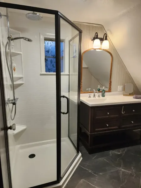 A bathroom with a black-framed corner shower stall, a dark wood vanity with a white countertop, mirror, and marble floor.