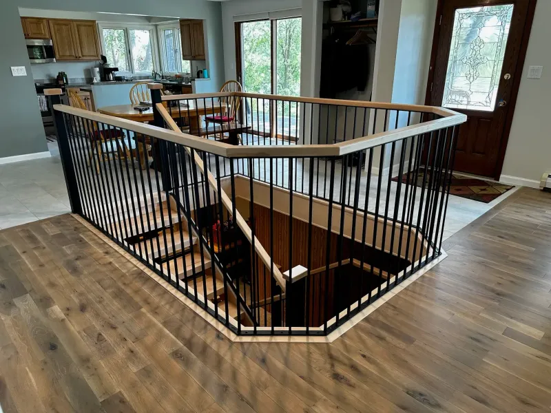 A wooden staircase opening features a modern black metal railing with a light wood handrail in a home with hardwood floors.