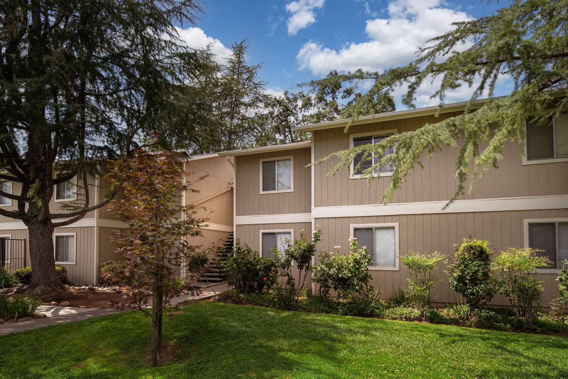 Apartment complex with beige siding, green lawn, and trees under a blue sky.