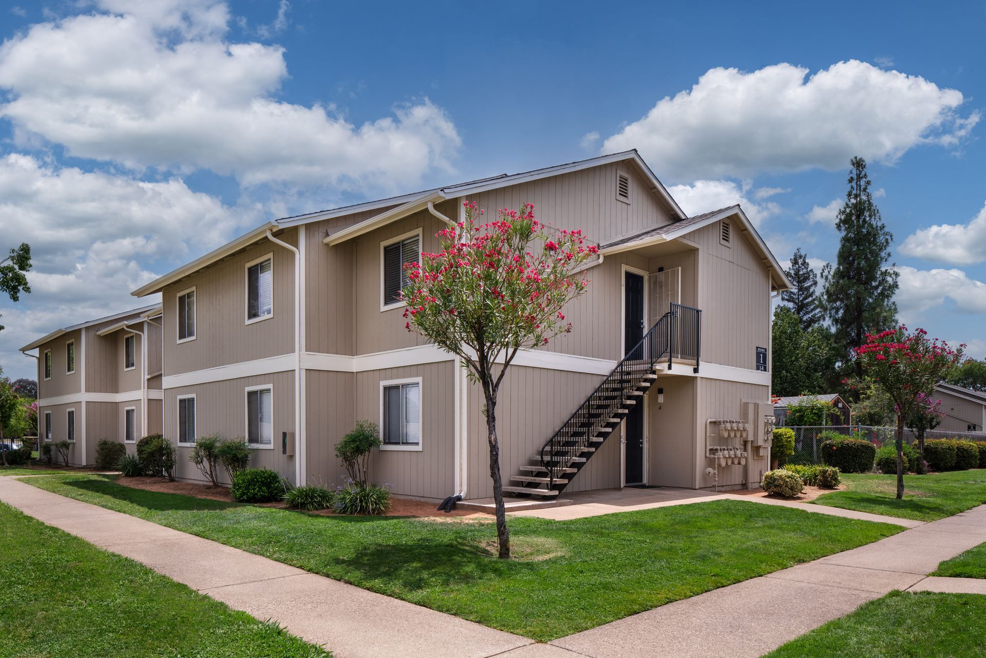 Two-story beige apartment building with a grassy lawn under a blue sky.