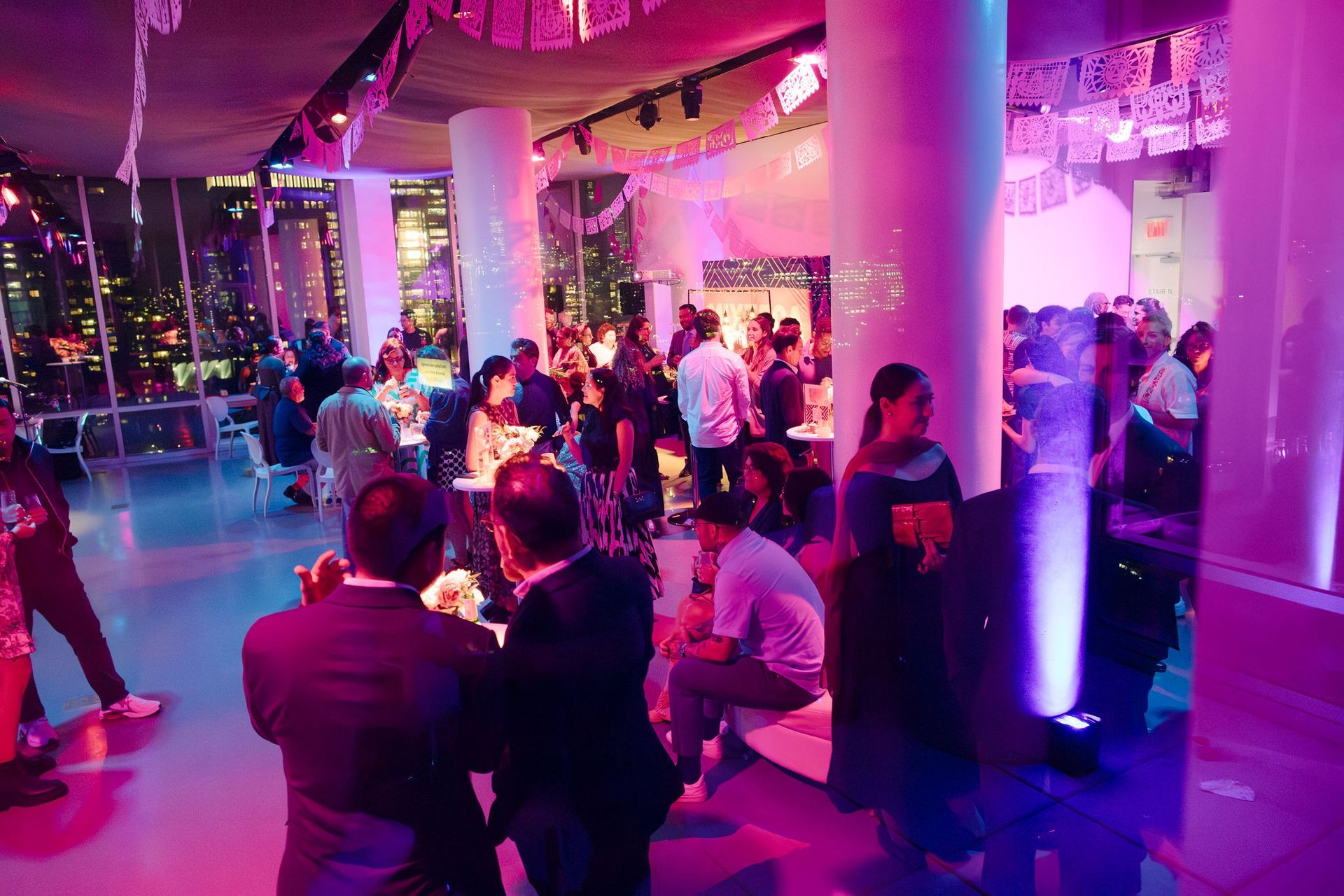 Restaurant interior with tables set for dinner, overlooking a lit-up cityscape at night.