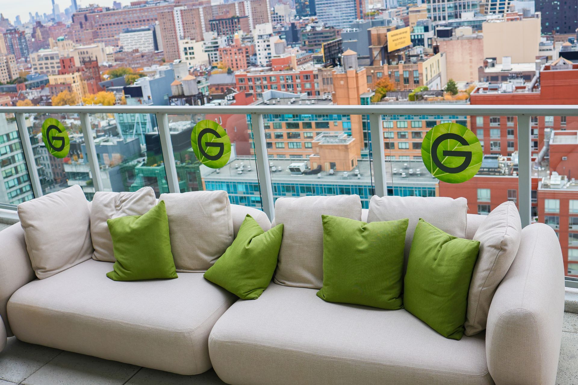 A white couch with green pillows sits on a balcony overlooking a city