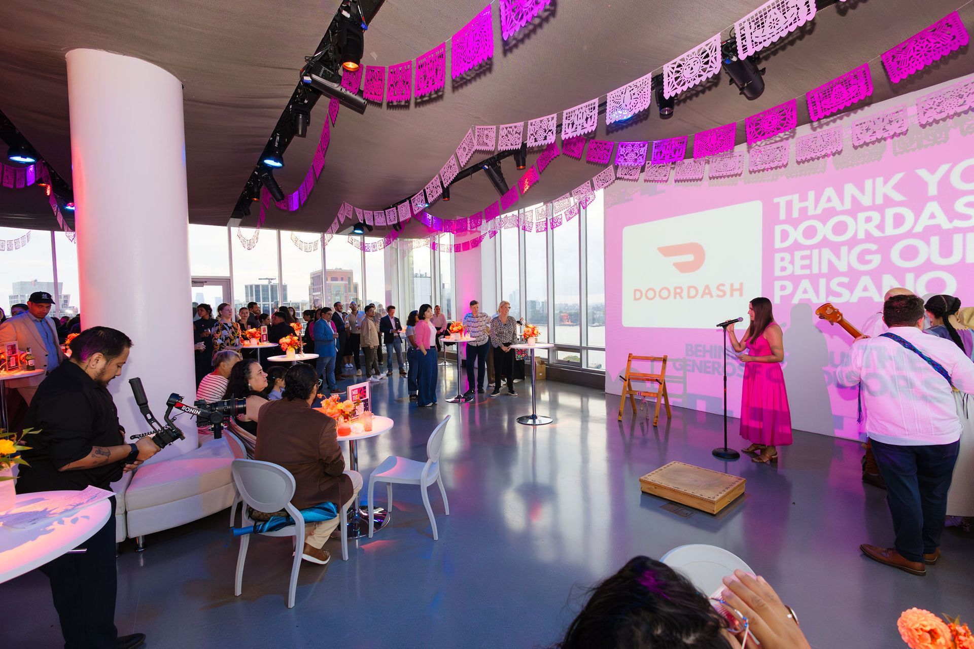 DoorDash event: People in a room with pink decorations, a stage, and a projected logo. Musicians perform.