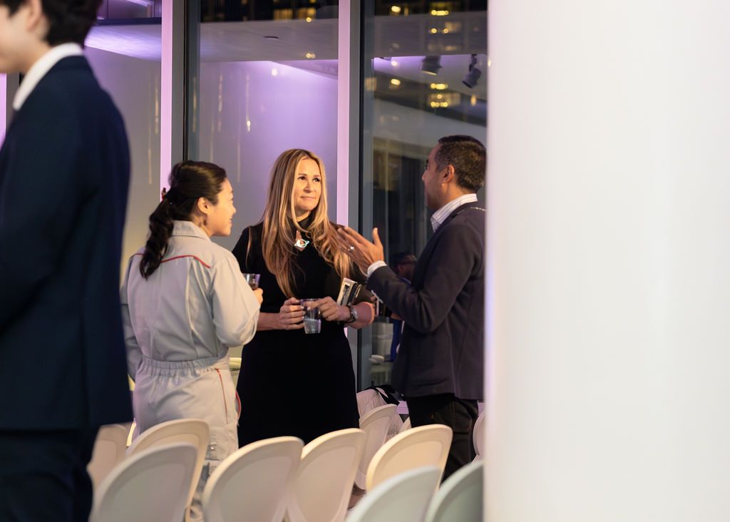 People socializing at an event with drinks, in a modern setting with chairs.