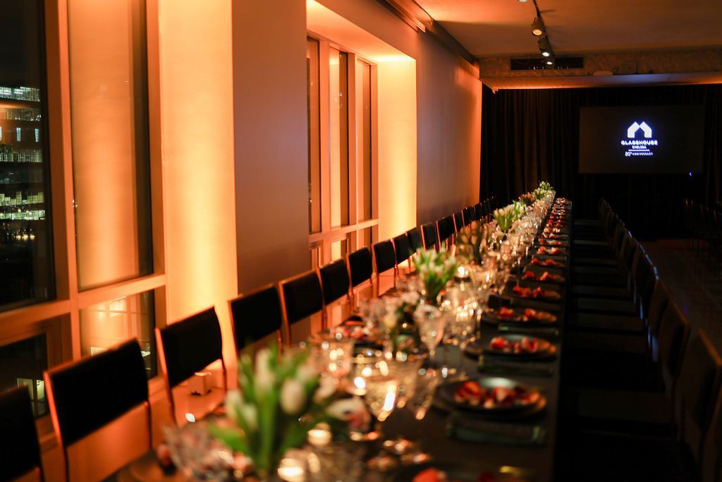 Long dining table set for a formal event, lit with warm orange light.