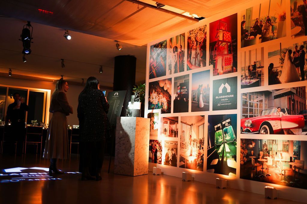 Two people stand near a wall covered with framed photos in a warmly lit gallery setting.