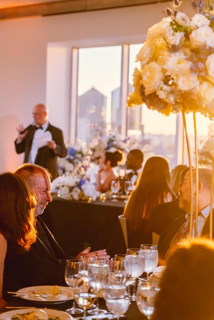 A man in a tuxedo is giving a speech at a wedding reception.