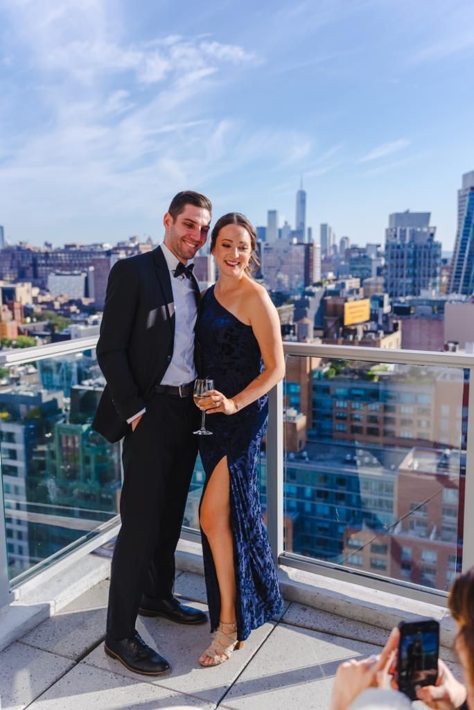 A man and a woman are posing for a picture on a balcony overlooking a city.