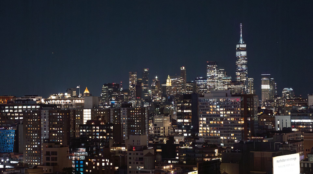 Nighttime view of a city skyline with illuminated skyscrapers under a dark blue sky.