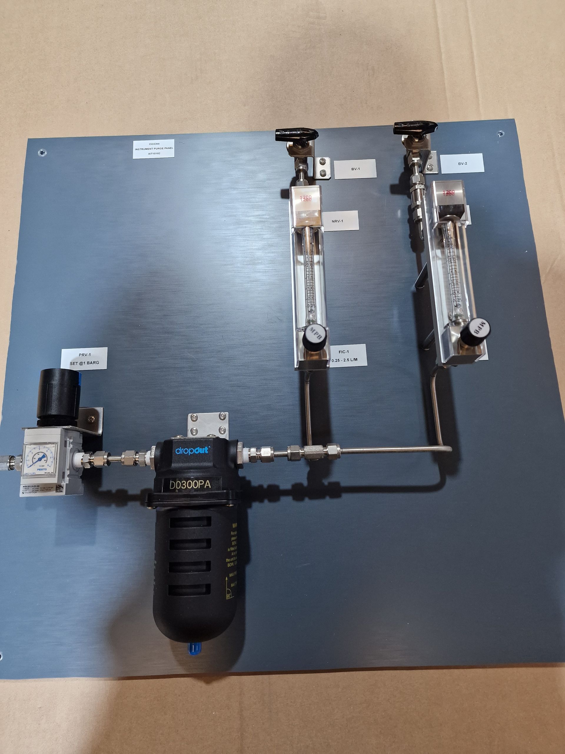 A pneumatic system board featuring a filter, solenoid valve, and two flow meters mounted on a dark grey panel.