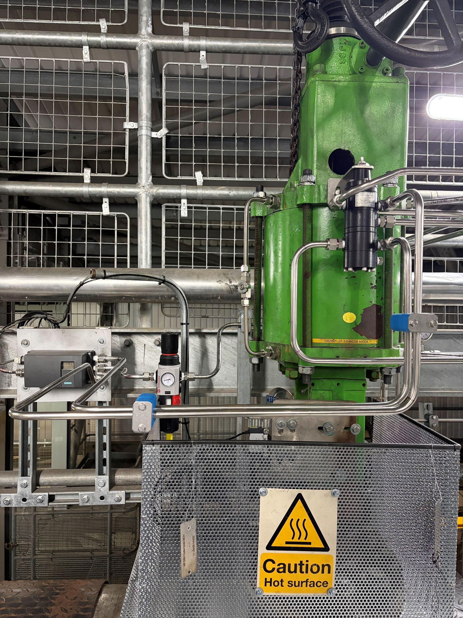 A stainless steel industrial instrument panel with pressure gauges, valves, tubing, and a flow meter mounted on a wall.
