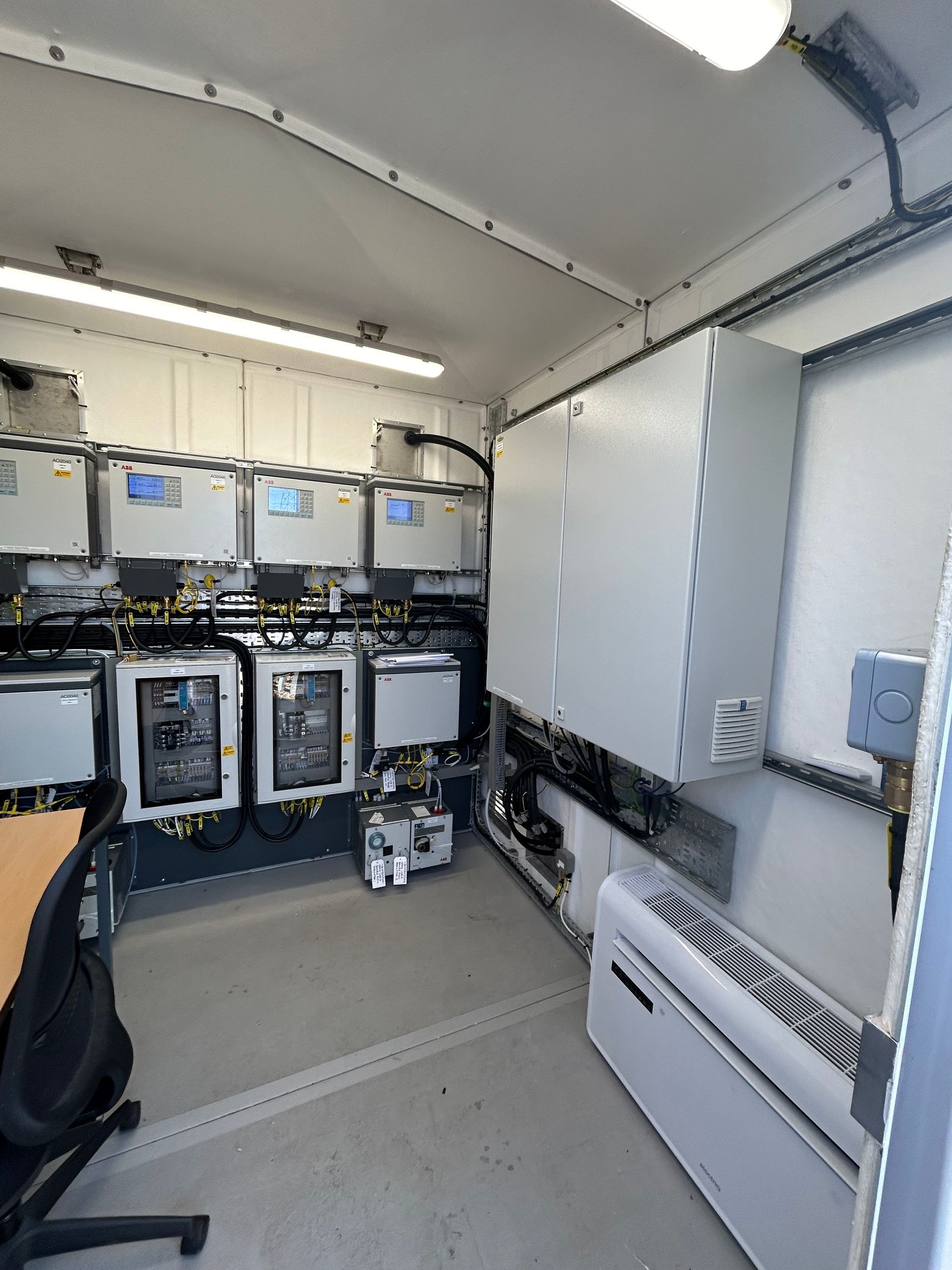 A small control room featuring a wall of electronic monitoring equipment, a large gray cabinet, and a wall-mounted heater.