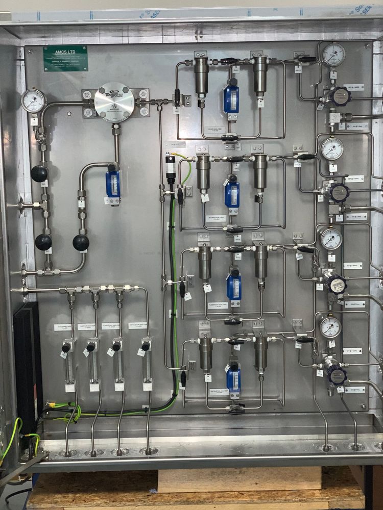 Industrial gas sampling and filtration panel featuring stainless steel piping, gauges, and blue filters mounted on a board.