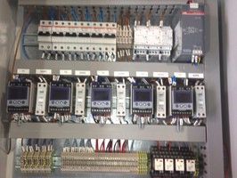 An electrical control panel with circuit breakers, digital controllers, and terminal blocks mounted on rails.