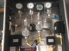 A wall-mounted industrial control panel featuring pressure gauges, piping, valves, and electrical enclosures.