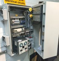 An open metal electrical control panel mounted on a wall, containing various switches, dials, and wiring components.