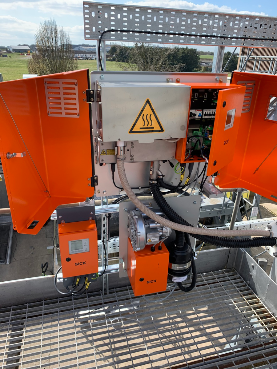 Open industrial equipment cabinets with orange panels, a hot surface warning sign, and internal wiring on a metal grate.