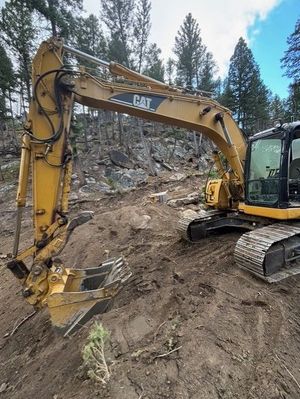 A yellow CAT excavator parked on a dirt slope in a wooded area.