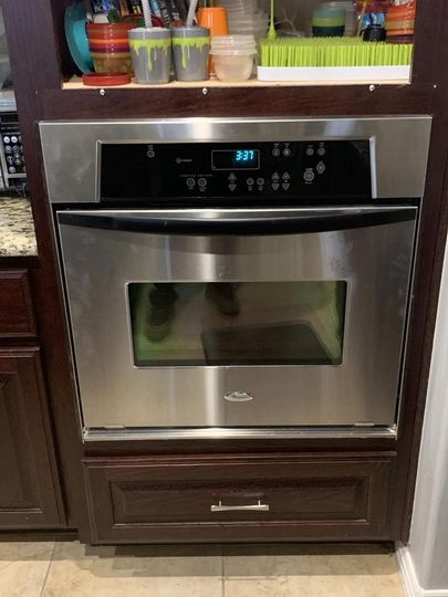 A stainless steel oven is sitting on top of a wooden cabinet in a kitchen.