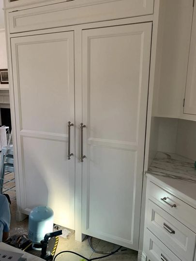 A kitchen with white cabinets , drawers , and a refrigerator.